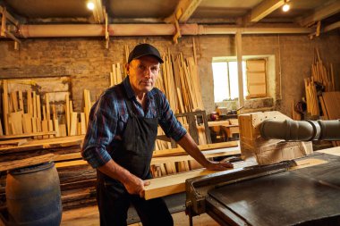 Elektrikli testere ile ahşap kesme masası. Kıdemli profesyonel marangoz üniformalı kereste fabrikasında ahşap tahta kesiyor. Testere makinesi