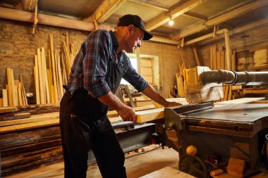 Elektrikli testere ile ahşap kesme masası. Kıdemli profesyonel marangoz üniformalı kereste fabrikasında ahşap tahta kesiyor. Testere makinesi