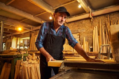 Elektrikli testere ile ahşap kesme masası. Kıdemli profesyonel marangoz üniformalı kereste fabrikasında ahşap tahta kesiyor. Testere makinesi