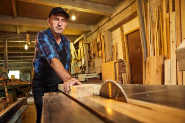 Elektrikli testere ile ahşap kesme masası. Kıdemli profesyonel marangoz üniformalı kereste fabrikasında ahşap tahta kesiyor. Testere makinesi