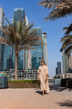 Dubai Marina bölgesinde uzun bir elbise giyen çekici bir gezgin kadın gezinti güvertesinde yürüyor. BAE 'de seyahat yerleri ve turist yaşam tarzı