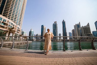 Dubai Marina bölgesinde uzun bir elbise giyen çekici bir gezgin kadın gezinti güvertesinde yürüyor. BAE 'de seyahat yerleri ve turist yaşam tarzı