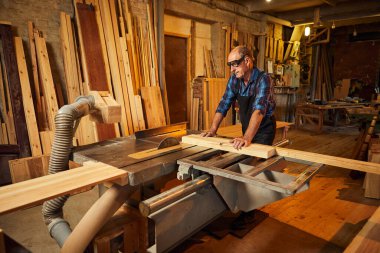 Elektrikli testere ile ahşap kesme masası. Kıdemli profesyonel marangoz üniformalı kereste fabrikasında ahşap tahta kesiyor. Testere makinesi