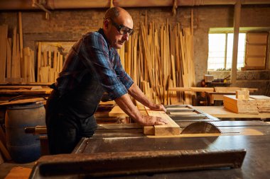 Elektrikli testere ile ahşap kesme masası. Kıdemli profesyonel marangoz üniformalı kereste fabrikasında ahşap tahta kesiyor. Testere makinesi