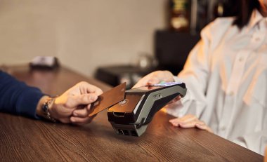 Müşterinin eli NFC teknolojisiyle temassız bir kredi kartı için ödeme yapıyor. Kredi kartı okuyucusu olan bir barmen. Ellere odaklan..