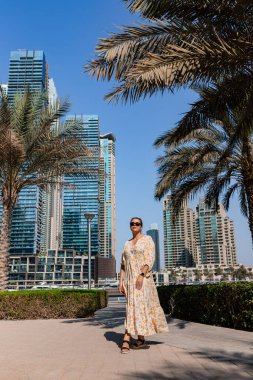 Dubai Marina bölgesinde uzun bir elbise giyen çekici bir gezgin kadın gezinti güvertesinde yürüyor. BAE 'de seyahat yerleri ve turist yaşam tarzı