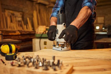 Kıdemli profesyonel marangoz üniformalı marangozluk atölyesinde elle değirmen makinesinde çalışıyor.