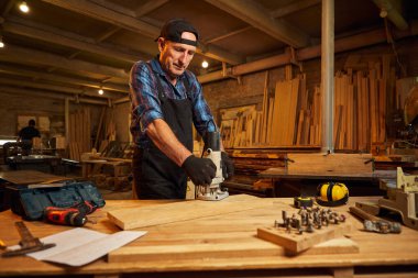 Kıdemli profesyonel marangoz üniformalı marangozluk atölyesinde elle değirmen makinesinde çalışıyor.