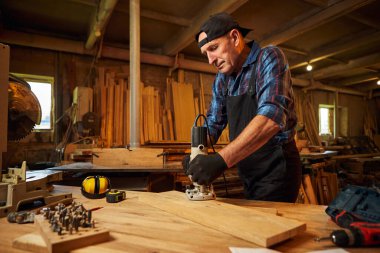 Kıdemli profesyonel marangoz üniformalı marangozluk atölyesinde elle değirmen makinesinde çalışıyor.