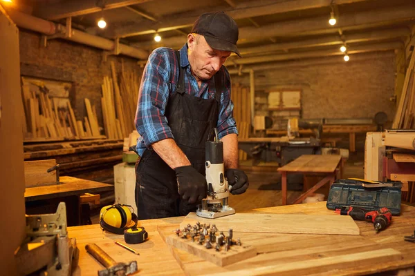 Kıdemli profesyonel marangoz üniformalı marangozluk atölyesinde elle değirmen makinesinde çalışıyor.