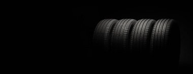Yeni araba lastikleri. Karanlık arka planda bir grup yol tekeri. Asimetrik lastik dizaynlı yaz lastikleri. Araba sürme kavramı.