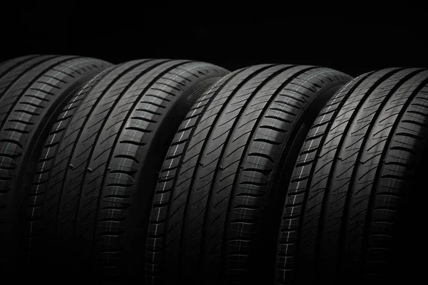 Yeni araba lastikleri. Karanlık arka planda bir grup yol tekeri. Asimetrik lastik dizaynlı yaz lastikleri. Araba sürme kavramı.