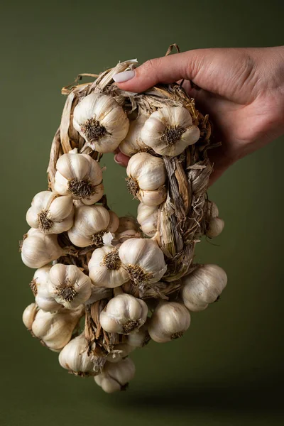 Bir kadının eli zeytin zemininde kokulu bir sarımsak çelengi tutar. Tarım ve tarım