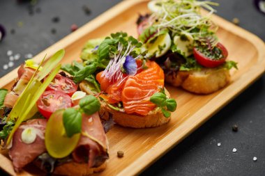 Somon, parma ve pesto soslu çeşitli bruschetta seti. İtalyan antipasti atıştırmalıkları. Koyu arkaplanda küçük sandviçlerin çeşitli karışımları. Restoran menüsü için fotoğraf