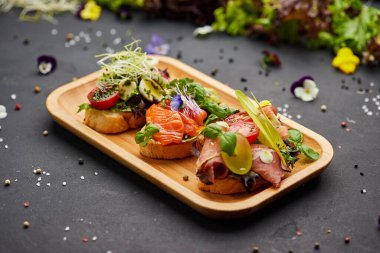 Somon, parma ve pesto soslu çeşitli bruschetta seti. İtalyan antipasti atıştırmalıkları. Koyu arkaplanda küçük sandviçlerin çeşitli karışımları. Restoran menüsü için fotoğraf