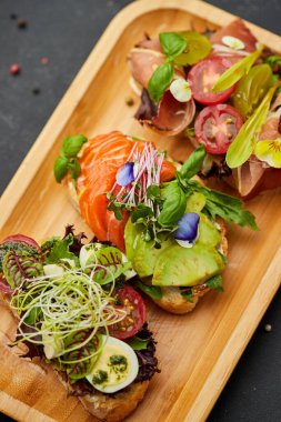 Somon, parma ve pesto soslu çeşitli bruschetta seti. İtalyan antipasti atıştırmalıkları. Koyu arkaplanda küçük sandviçlerin çeşitli karışımları. Restoran menüsü için fotoğraf