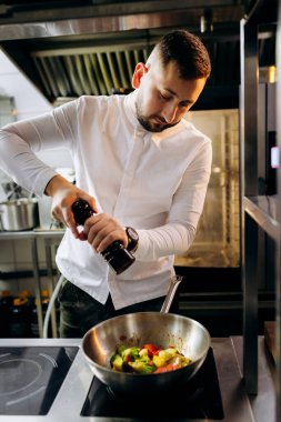 Profesyonel mutfakta, elinde tava ve ateşle. Şefin elleri demir tepsiyi tutuyor ve yemek pişiriyor..