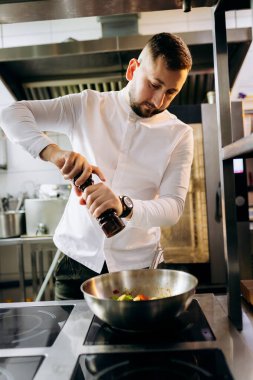 Profesyonel mutfakta, elinde tava ve ateşle. Şefin elleri demir tepsiyi tutuyor ve yemek pişiriyor..