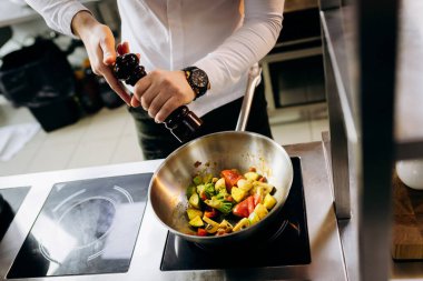 Profesyonel mutfakta, elinde tava ve ateşle. Şefin elleri demir tepsiyi tutuyor ve yemek pişiriyor..