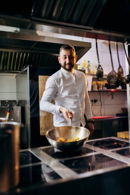 Profesyonel mutfakta, elinde tava ve ateşle. Şefin elleri demir tepsiyi tutuyor ve yemek pişiriyor..