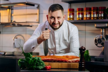 Mutfakta çiğ et pişiren yakışıklı şefin portresi. Elinde profesyonel bir mutfak bıçağı var. Yemek pişirme ve yemek hazırlama kavramı