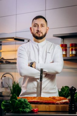 Mutfakta çiğ et pişiren yakışıklı şefin portresi. Elinde profesyonel bir mutfak bıçağı var. Yemek pişirme ve yemek hazırlama kavramı