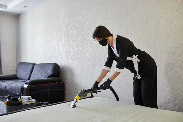 Cleaning service company employee removing dirt from furniture in flat with professional equipment. Woman housewife cleaning the mattress on the bed with a washing vacuum cleaner