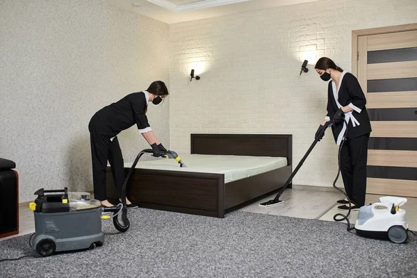 Cleaning company employees remove dirt from furniture in the apartment using professional equipment. Housewife women cleaning the mattress and floor with washing and steam vacuum cleaners