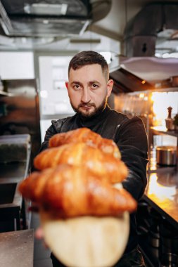 Fırında yeni pişmiş kruvasan tutan üniformalı yakışıklı fırıncı.