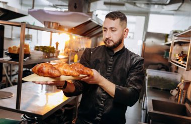 Fırında yeni pişmiş kruvasan tutan üniformalı yakışıklı fırıncı.