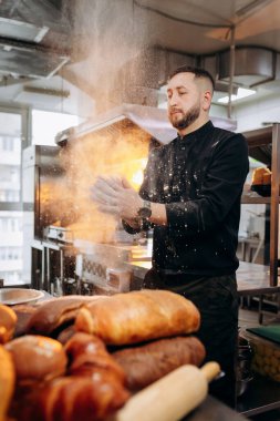 Unlu bir şef. Üniformalı yakışıklı fırıncı fırında ekmek ya da kruvasan pişirdiği için un vuruyor.