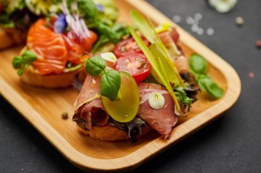 Somon, parma ve pesto soslu çeşitli bruschetta seti. İtalyan antipasti atıştırmalıkları. Koyu arkaplanda küçük sandviçlerin çeşitli karışımları. Restoran menüsü için fotoğraf