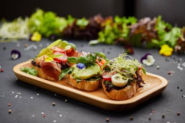 Somon, parma ve pesto soslu çeşitli bruschetta seti. İtalyan antipasti atıştırmalıkları. Koyu arkaplanda küçük sandviçlerin çeşitli karışımları. Restoran menüsü için fotoğraf