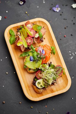 Somon, parma ve pesto soslu çeşitli bruschetta seti. İtalyan antipasti atıştırmalıkları. Koyu arkaplanda küçük sandviçlerin çeşitli karışımları. Restoran menüsü için fotoğraf