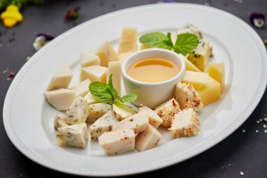 Peynir tabağı: parmesan, çedar, gouda, mozzarella ve diğer koyu arkaplanda beyaz tabakta bal. Lezzetli aperatifler. Üst Manzara. Restoran menüsü için fotoğraf