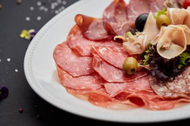Soğuk et tabağı, jambon, sosis, salam, parma, prosciutto, koyu arkaplanda salam ve zeytin ile kesilmiş domuz pastırması. Et aperatifi, şarap seti, yakın çekim.