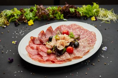 Soğuk et tabağı, jambon, sosis, salam, parma, prosciutto, koyu arkaplanda salam ve zeytin ile kesilmiş domuz pastırması. Et aperatifi, şarap seti, yakın çekim.