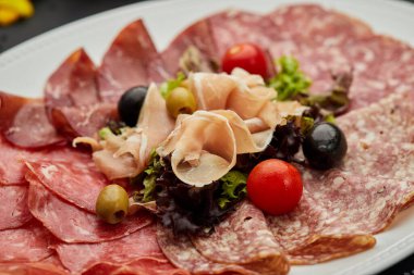 Soğuk et tabağı, jambon, sosis, salam, parma, prosciutto, koyu arkaplanda salam ve zeytin ile kesilmiş domuz pastırması. Et aperatifi, şarap seti, yakın çekim.