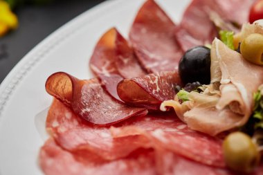 Soğuk et tabağı, jambon, sosis, salam, parma, prosciutto, koyu arkaplanda salam ve zeytin ile kesilmiş domuz pastırması. Et aperatifi, şarap seti, yakın çekim.