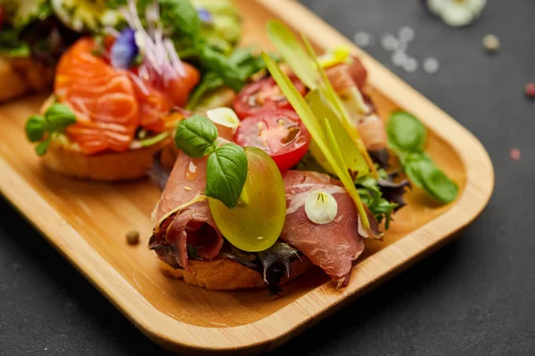 Somon, parma ve pesto soslu çeşitli bruschetta seti. İtalyan antipasti atıştırmalıkları. Koyu arkaplanda küçük sandviçlerin çeşitli karışımları. Restoran menüsü için fotoğraf