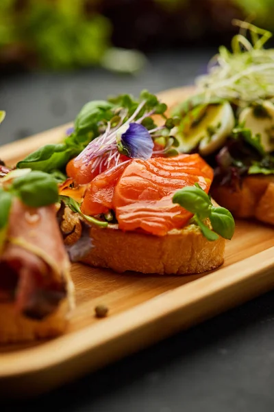 Somon, parma ve pesto soslu çeşitli bruschetta seti. İtalyan antipasti atıştırmalıkları. Koyu arkaplanda küçük sandviçlerin çeşitli karışımları. Restoran menüsü için fotoğraf