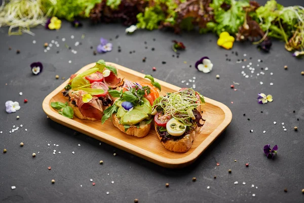 Somon, parma ve pesto soslu çeşitli bruschetta seti. İtalyan antipasti atıştırmalıkları. Koyu arkaplanda küçük sandviçlerin çeşitli karışımları. Restoran menüsü için fotoğraf