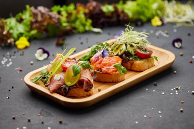 Somon, parma ve pesto soslu çeşitli bruschetta seti. İtalyan antipasti atıştırmalıkları. Koyu arkaplanda küçük sandviçlerin çeşitli karışımları. Restoran menüsü için fotoğraf