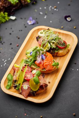 Somon, parma ve pesto soslu çeşitli bruschetta seti. İtalyan antipasti atıştırmalıkları. Koyu arkaplanda küçük sandviçlerin çeşitli karışımları. Restoran menüsü için fotoğraf