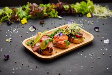 Somon, parma ve pesto soslu çeşitli bruschetta seti. İtalyan antipasti atıştırmalıkları. Koyu arkaplanda küçük sandviçlerin çeşitli karışımları. Restoran menüsü için fotoğraf