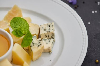 Peynir tabağı: parmesan, çedar, gouda, mozzarella ve diğer koyu arkaplanda beyaz tabakta bal. Lezzetli aperatifler. Üst Manzara. Restoran menüsü için fotoğraf