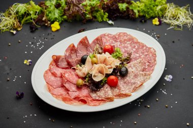 Soğuk et tabağı, jambon, sosis, salam, parma, prosciutto, koyu arkaplanda salam ve zeytin ile kesilmiş domuz pastırması. Et aperatifi, şarap seti, yakın çekim.