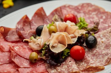 Soğuk et tabağı, jambon, sosis, salam, parma, prosciutto, koyu arkaplanda salam ve zeytin ile kesilmiş domuz pastırması. Et aperatifi, şarap seti, yakın çekim.