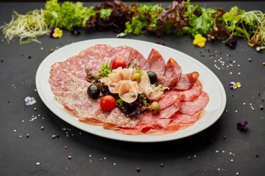 Soğuk et tabağı, jambon, sosis, salam, parma, prosciutto, koyu arkaplanda salam ve zeytin ile kesilmiş domuz pastırması. Et aperatifi, şarap seti, yakın çekim.