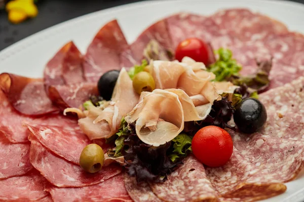 Soğuk et tabağı, jambon, sosis, salam, parma, prosciutto, koyu arkaplanda salam ve zeytin ile kesilmiş domuz pastırması. Et aperatifi, şarap seti, yakın çekim.
